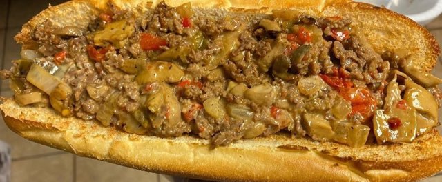A close-up of an overstuffed cheesesteak with peppers and mushrooms